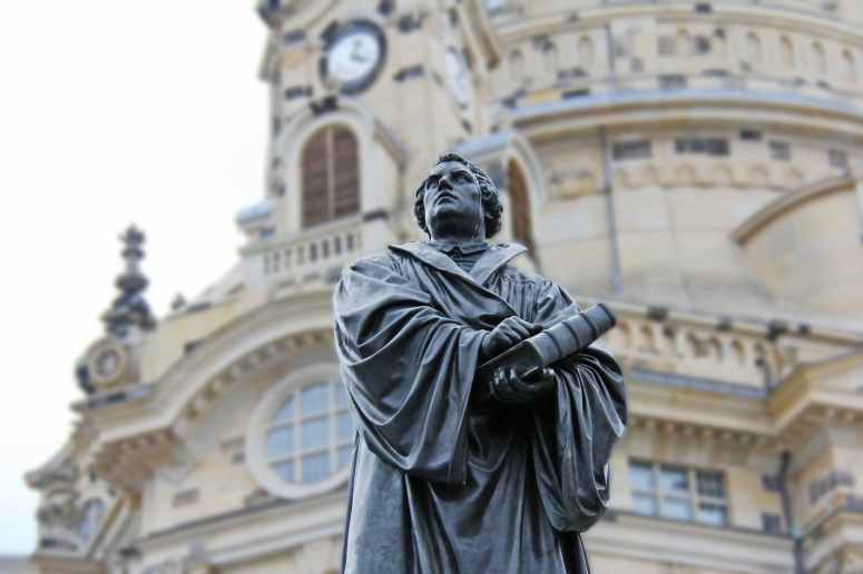 gray concrete statue of man holding book beside brown building